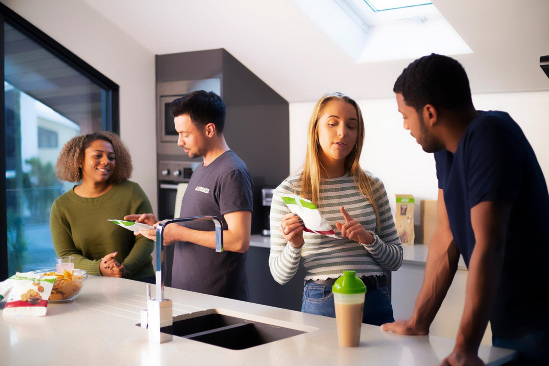 Group of people chatting in a kitchen while preparing or sharing food and drinks.