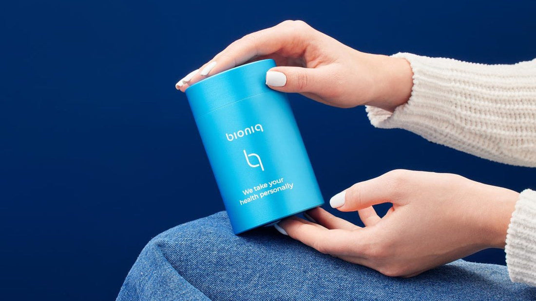 Person holding Bioniq skincare product against blue background indoors